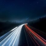 Long exposure night shot capturing stunning red and white light trails on a highway under a starry sky.